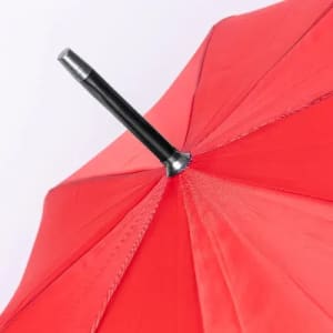 A red umbrella seen from above, featuring a black handle and a metal tip at the centre.
