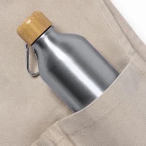 A drink bottle with a stainless steel finish and a bamboo lid, placed in a beige fabric pocket.