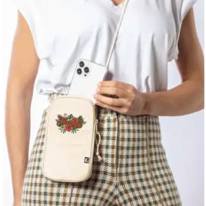 A phone pouch in cream with floral embroidery, worn crossbody with a phone being placed inside.