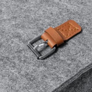 A leather strap with a metal buckle rests on a grey felt background.