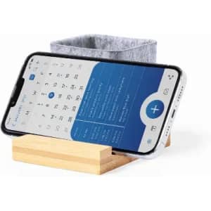 A phone in a wooden stand, displaying a calendar app, next to a grey felt container.