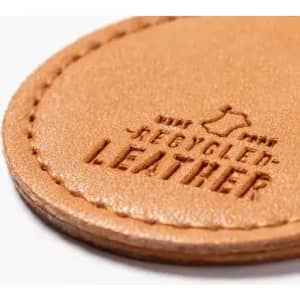 A close-up of a light brown recycled leather patch featuring embossed text. The patch has a stitched edge.