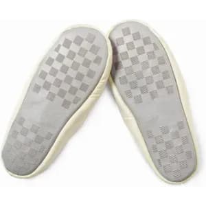 A pair of cream-coloured slip-on shoes with a checkered patterned sole. The shoes are lightweight and soft.