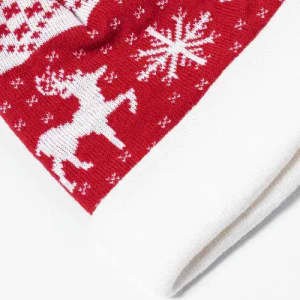 A red knitted Christmas stocking featuring white patterns of a reindeer and snowflakes, with a white cuff at the top.