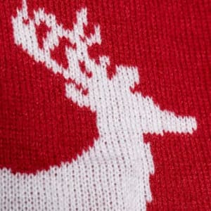 A close-up of a red fabric featuring a white reindeer silhouette in a knitted pattern.