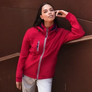 A woman poses in a red jacket with a hood, featuring zippered pockets and a sleek design against a brown background.