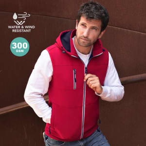 A red sleeveless jacket with a hood, featuring a zip-front and pockets, set against a rustic background.