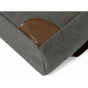 A grey cushion featuring a brown leather accent on one corner. The fabric has a textured finish.