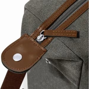 A close-up of a grey fabric bag featuring a brown leather zipper pull and strap, showcasing detailed stitching.