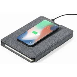 A grey notebook with a smartphone charging on top, connected by a cable. The notebook features a textured cover.