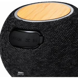 A round speaker with a textured black fabric exterior and a bamboo top. It features an on/off switch.