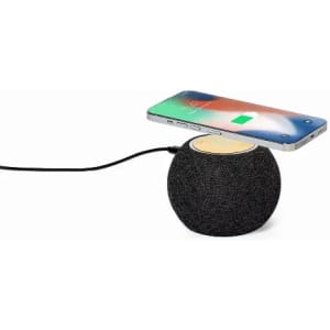 A wireless charging speaker in dark grey with a wood-accented top, featuring a smartphone charging above it.