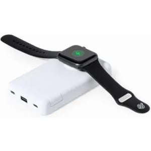 A black smartwatch rests on a white charging pad, with USB ports visible on one side. The pad has a minimalist design.