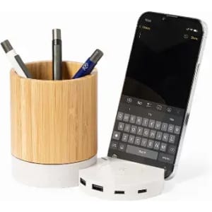 A bamboo pen holder with pens and a smartphone on a white charging base with multiple USB ports.
