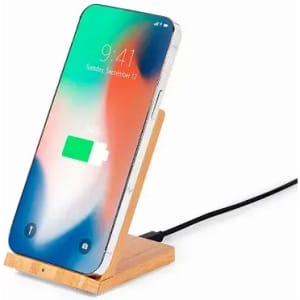 A smartphone on a wooden charging stand, connected to a power cable, displaying a battery charging icon.