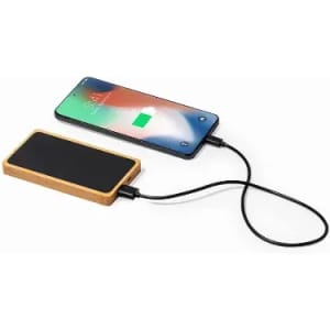 A power bank with a wooden exterior connected to a smartphone, charging it. The smartphone displays a charging icon.