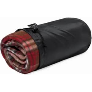 A rolled blanket with a red and brown plaid pattern, wrapped in a black storage bag. It features a logo on the bag.