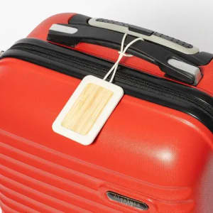 A red suitcase features a rectangular luggage tag with a wooden design attached to the handle.
