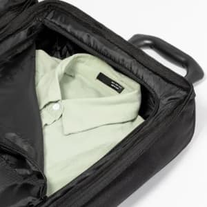 A black bag containing a folded light green shirt, zipped partially open to reveal its contents.