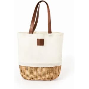 A cream tote bag with a woven wicker base and brown leather handles. It features a simple design and logo.
