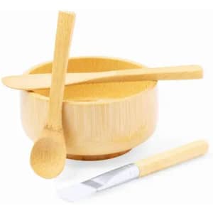A bamboo bowl with two wooden utensils and a flat-edged tool, all in natural wood tones. The bowl has a smooth finish.