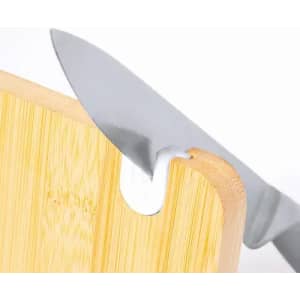A knife sits in a groove on a wooden cutting board, showcasing a sleek stainless steel blade and natural bamboo surface.