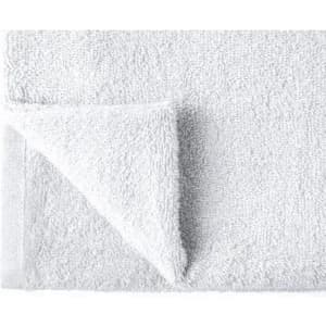 A white bath towel folded at one corner, featuring a textured surface and a neat edge. It includes a logo.