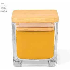 A glass jar with a bamboo lid, filled with yellow contents. The jar has a square shape and a minimalist design.