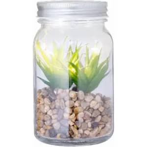 A glass jar containing decorative pebbles and artificial green plants, with light enhancing its appearance.