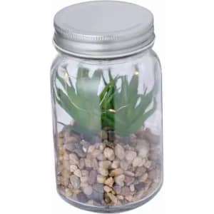 A glass jar contains artificial greenery and small pebbles, topped with a metallic lid.