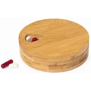 A round bamboo pill box with a small opening, featuring two capsules outside in red and white.