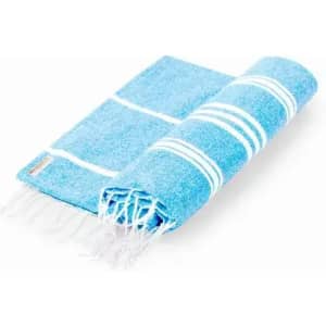 A blue beach towel with white stripes and fringed edges, folded neatly. It features a small logo.