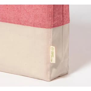 A tote bag with a pink top section and a cream bottom, featuring a small tag indicating recycled materials.