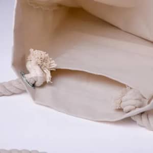 A cream-coloured tote bag with a rope handle and two decorative knots at the opening.