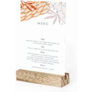 A menu card displayed on a wooden stand, featuring floral designs and various food categories like salads, soups, and desserts.