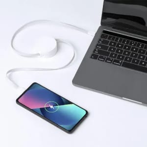 A smartphone with a charging cable connected to a laptop, featuring a circular charging pad. The devices are on a white surface.