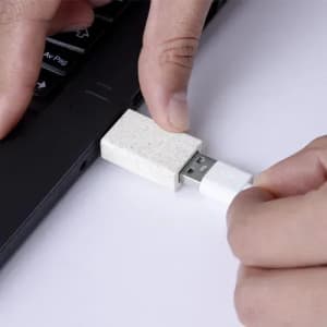 A USB drive with a textured, cream-coloured casing is being plugged into a laptop.