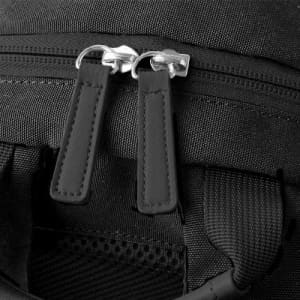 A close-up of black zippers on a textured fabric bag, featuring leather pull tabs and a detailed stitching design.