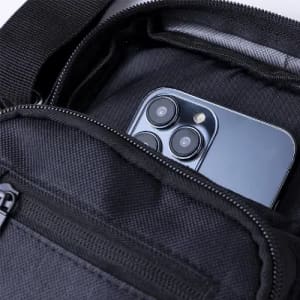 A black bag with a zipped pocket containing a smartphone. The bag has a textured surface and a simple design.