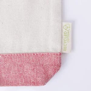 A fabric item with a cream body and a red-textured bottom edge, featuring a recycled cotton tag.