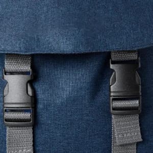 A backpack flap in dark blue fabric featuring black plastic buckles and grey straps.