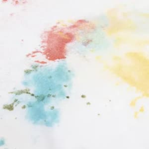 A textured surface featuring splashes of blue, red, green, and yellow colours on a white background.
