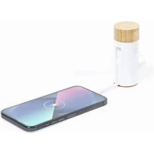 A white wireless charger with a bamboo top next to a black smartphone, both on a light surface.