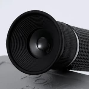 A black telescope with textured grip and a circular lens, resting on a flat surface.