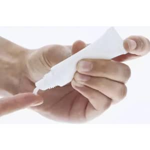 A hand holding a small white tube, dispensing its contents onto a fingertip. The tube has a plain design.