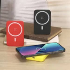 A powerbank trio in red, black, and yellow, with a phone charging wirelessly on a surface.