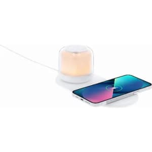 A wireless charging station with a soft, glowing lamp and a smartphone on a white surface. The light is orange and the product has a modern design.