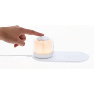 A light diffuser with a transparent dome and white base, emitting a warm glow, and being touched by a hand.