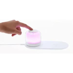 A light device with a transparent dome and a pink glow, operated by a hand pressing a button on a base.