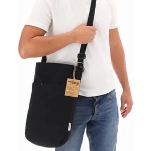 A black messenger bag with a long strap, featuring two pockets and a tag attached, being held by a person.